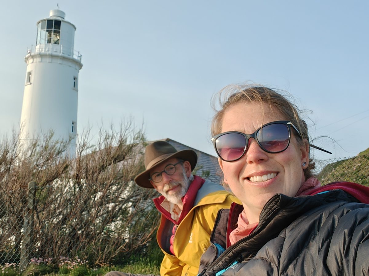 Lieke en haar vader Ben lachen in de camera, met een witte vuurtoren op de achtergrond